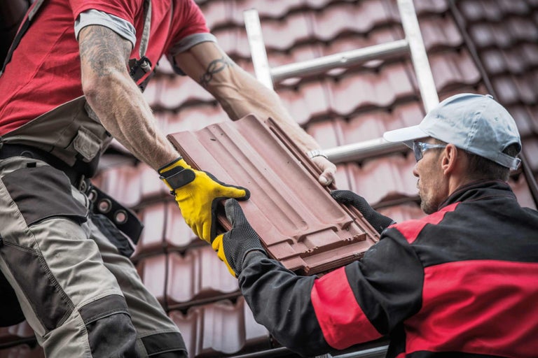 Dva pokrývači pokládají střešní tašky na střechu.