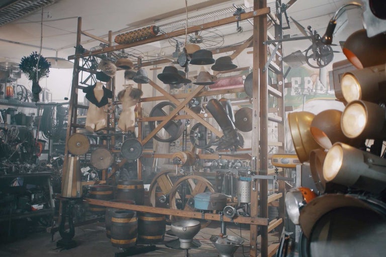 Scéna s klobouky, oblečením, sudy, koly a světlomety na dřevěné konstrukci v místnosti.