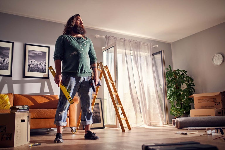 Světlá místnost během renovace s řemeslníkem, vodováhou, žebříkem a stěhovacími krabicemi