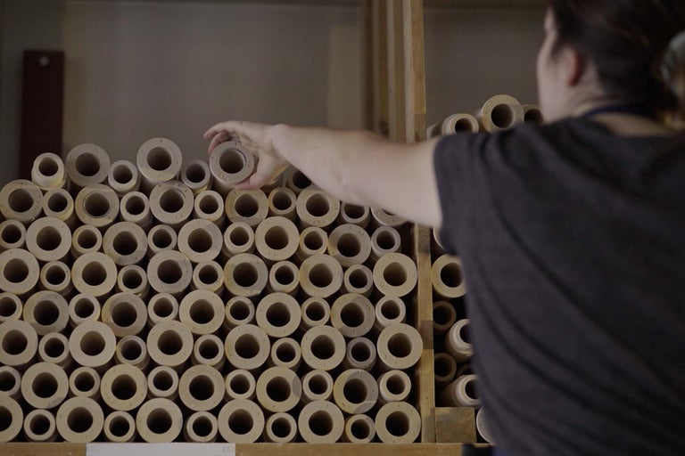 Snímek kulatých dřevěných distančních prvků naskládaných v regálu, přičemž jedna osoba distanční prvek vyjímá.