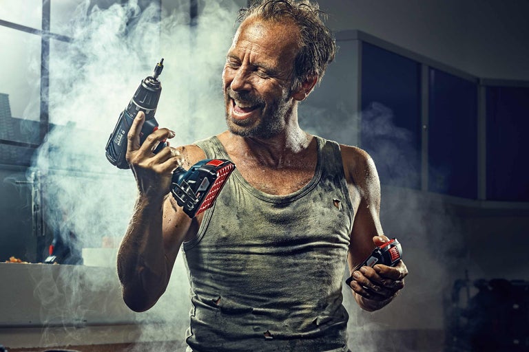 Řemeslník drží v ruce akumulátorový šroubovák a akumulátor