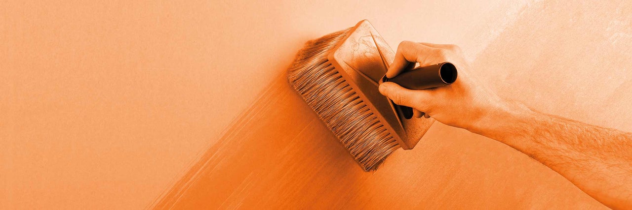 Osoba nanáší lazurovací štětec na stěnu