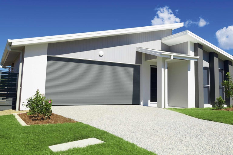 Moderní dům s šedou rolovací garáží, dlážděnou cestou a udržovanou zahradou.