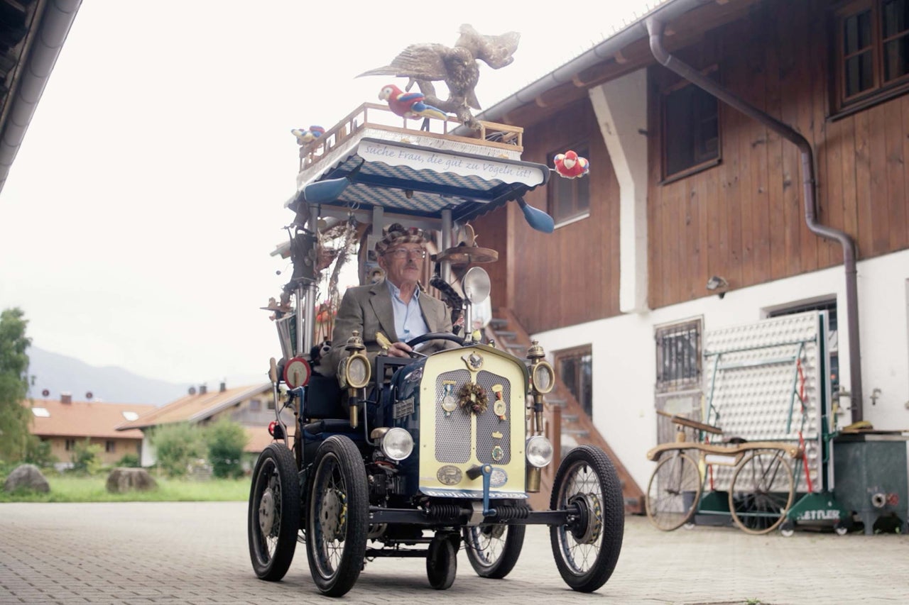 Muž řídí ozdobené auto s ptačími motivy před domem.