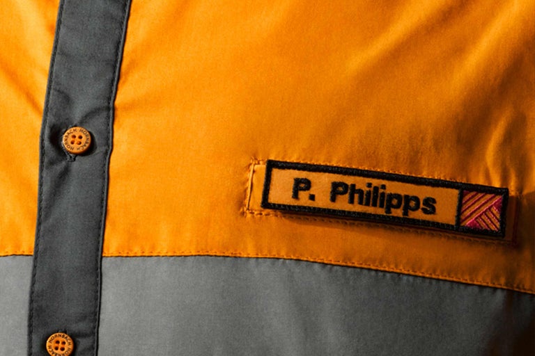 Detailní záběr pracovní košile s jmenovkou a logem Hornbach na knoflících