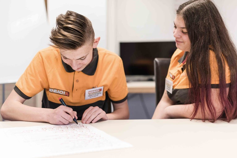 Dva zaměstnanci společnosti Hornbach sedí u stolu. Jeden z nich píše něco na list papíru.