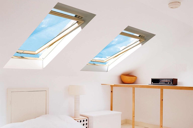 Dvě střešní okna osvětlují podkrovní pokoj s postelí a nábytkem.