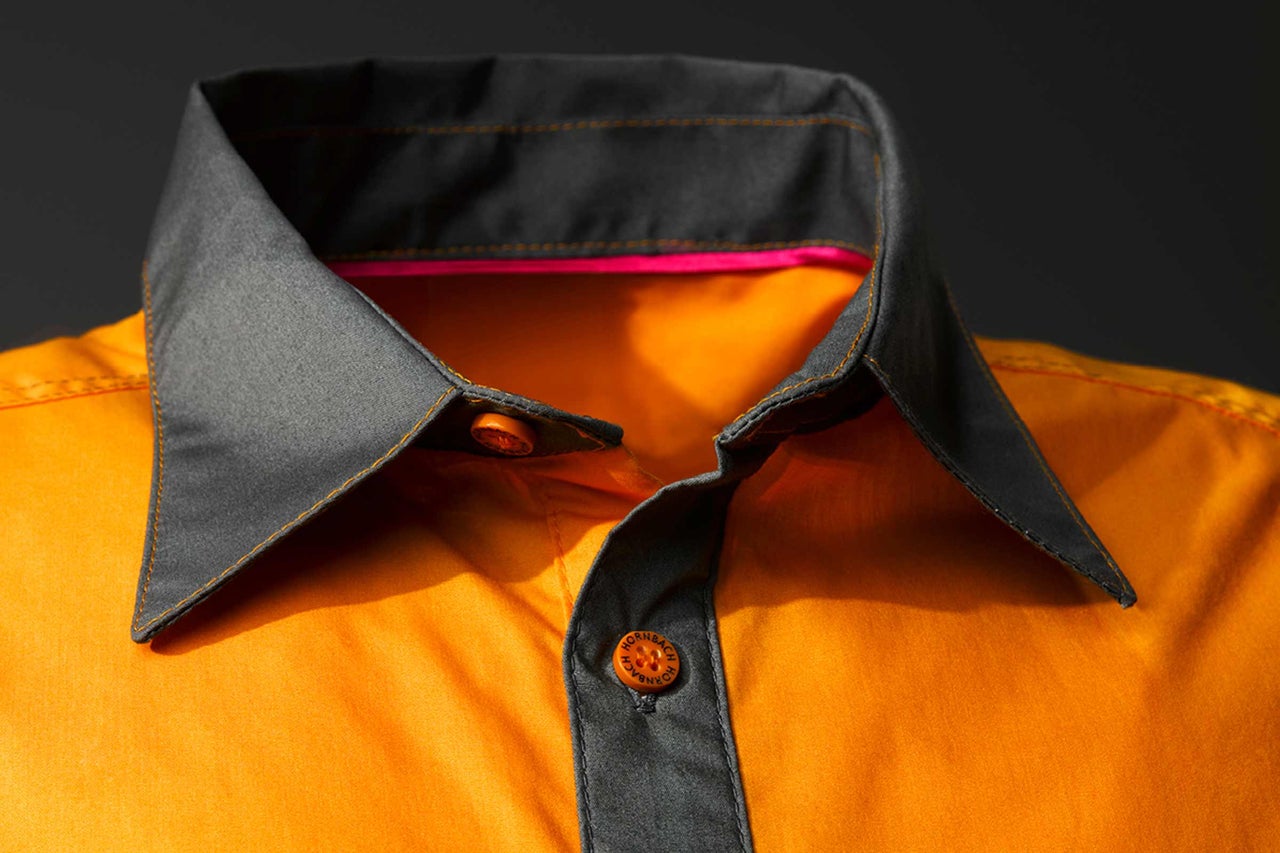 Detail oranžové pracovní košile s šedým límcem a logem Hornbach na knoflících.