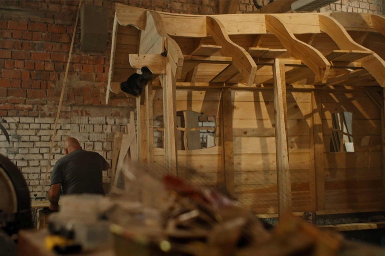 Nedokončený dřevěný dům v hrubé stavbě s pracovníkem v pozadí.