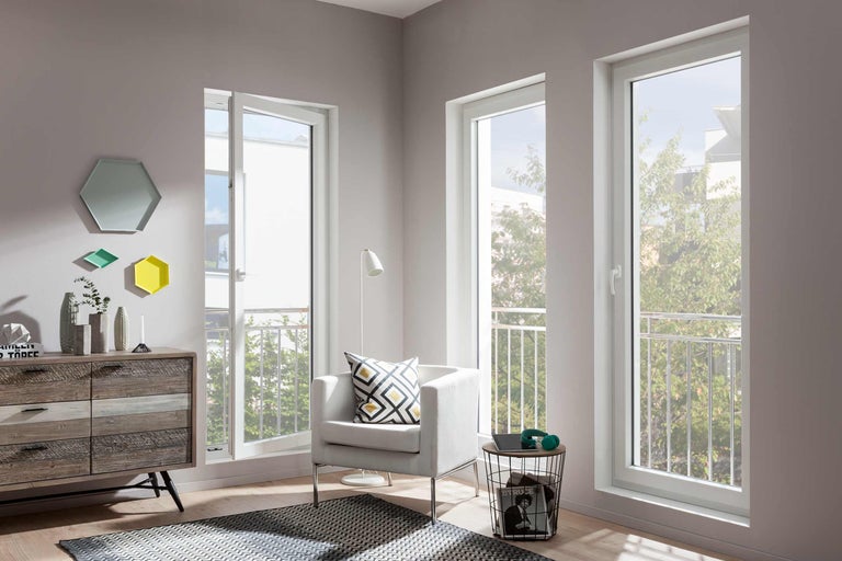 Světlý obývací pokoj s bílými plastovými okny, křeslem a komodou