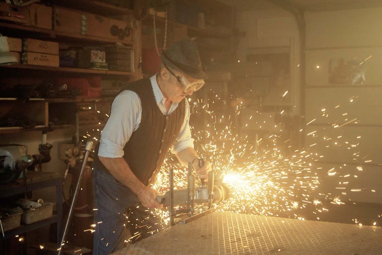 Muž v ochranných brýlích opracovává kov úhlovou bruskou, z které odlétávají jiskry.