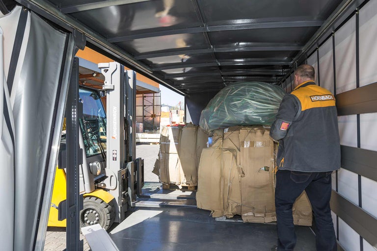 Vysokozdvižný vozík nakládá náklad do nákladního auta. Vedle stojí zaměstnanec společnosti Hornbach.