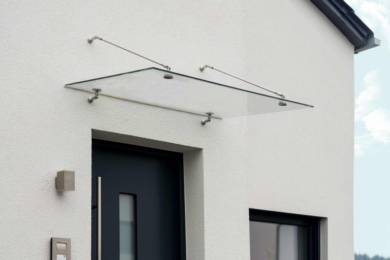 Skleněný baldachýn nad vchodovými dveřmi s nerezovými držáky na stěně domu