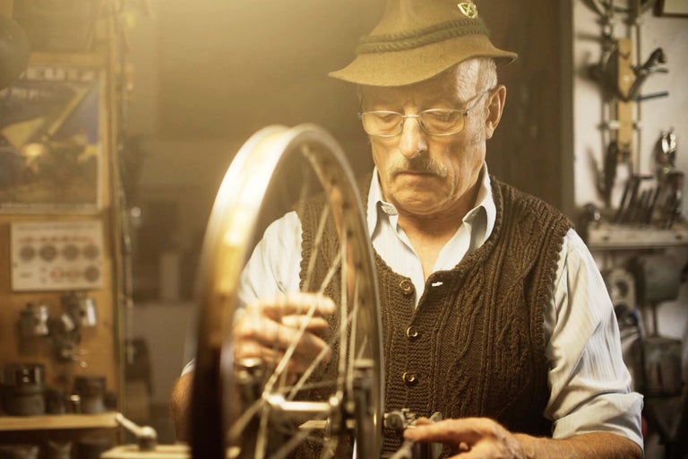 Muž s kloboukem opravuje kolo v dílně.