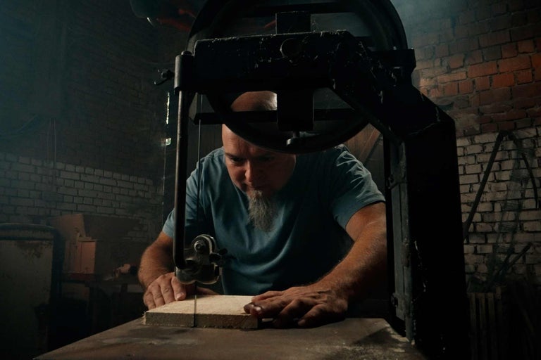 Muž řeže dřevo pásovou pilou