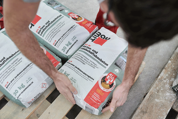 Osoba manipuluje s pytli zahradního a terénního betonu na paletě