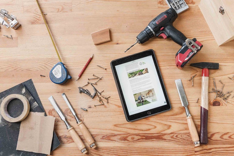 Pohled shora na pracovní stůl s nářadím, tabletem a stavebními materiály