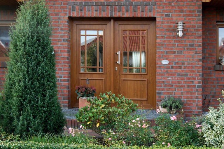 Dvojité dřevěné dveře se skleněnými výplněmi v červené cihlové fasádě obklopené rostlinami