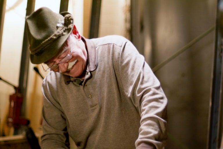 Muž s tradičním kloboukem a polokošilí se ohýbá dolů