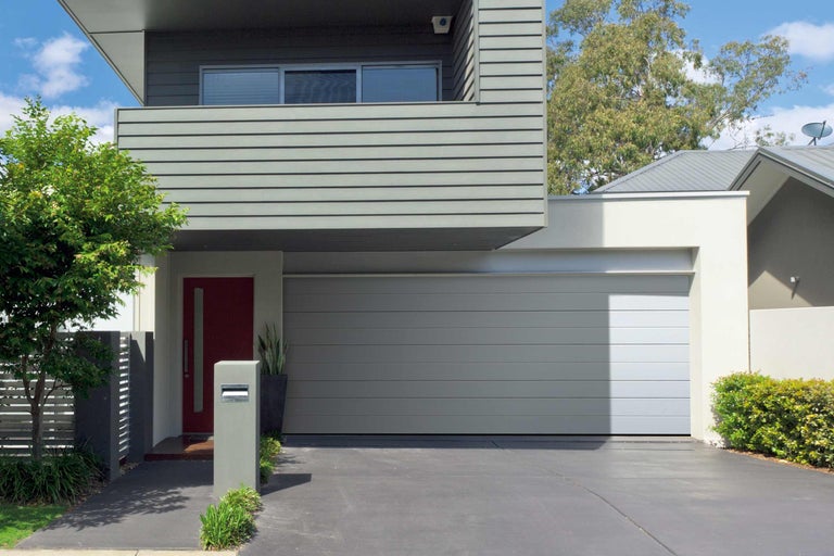 Moderní dům s šedou garáží a červenými vchodovými dveřmi.