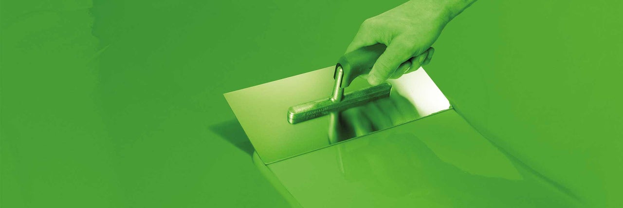 Ruka drží hladítko při nanášení potěru.