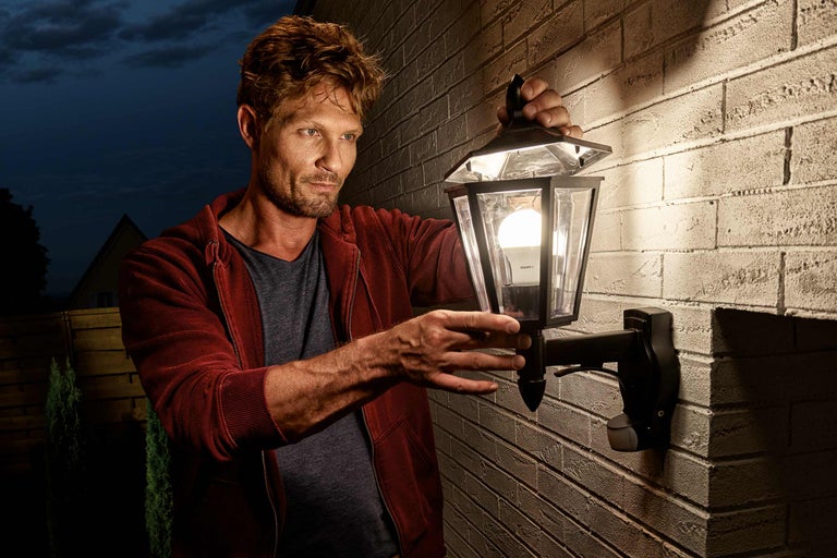 Muž montuje venkovní světlo na kamennou zeď