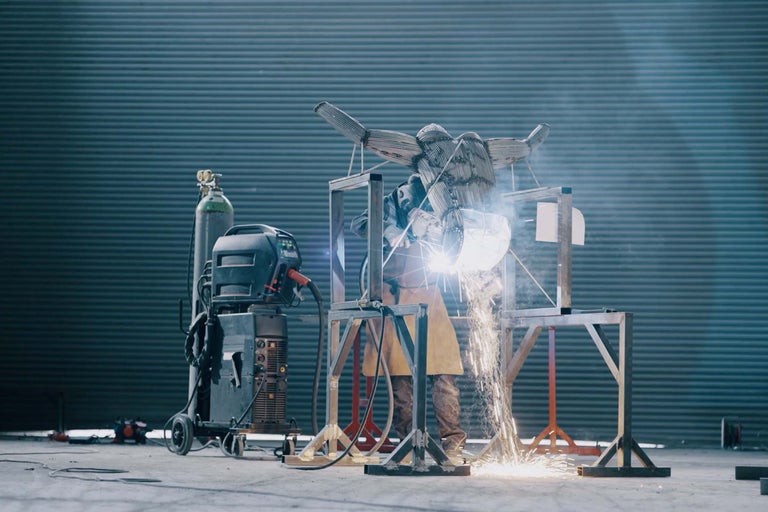 Svářeč pracuje na kovové soše se svařovacím zařízením