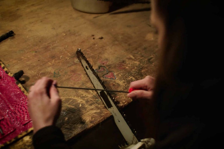 Osoba brousí řetězovou pilu s ostřicím nástrojem na pracovním stole.