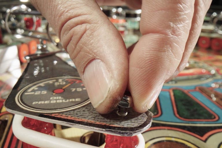 Osoba připevňuje kryt s ukazatelem tlaku oleje na flipper.