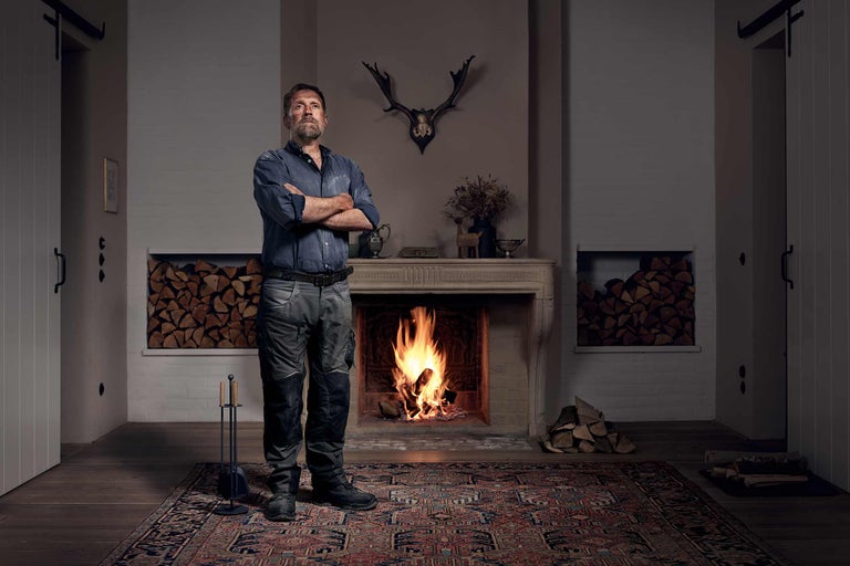 Muž v pracovním oděvu před krbem s hořícím ohněm