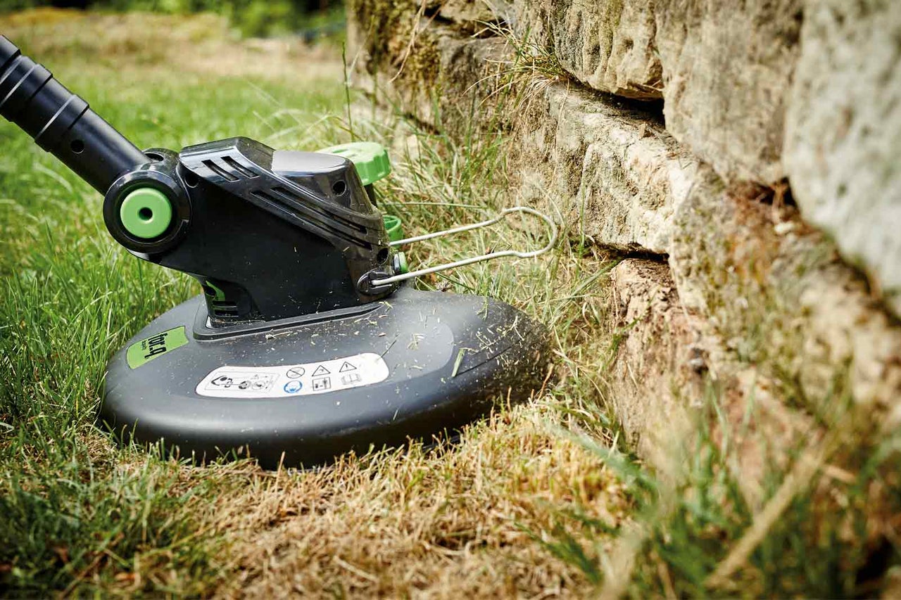 Zastřihovač trávy v provozu u kamenné zdi