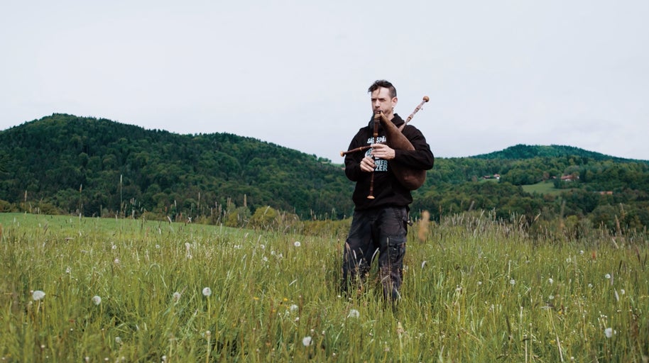 Muž s dudami na louce se stromy v pozadí