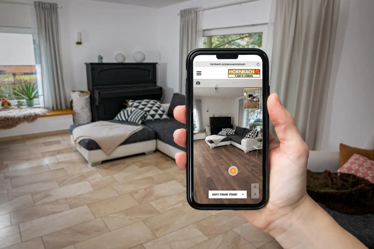 Osoba drží smartphone s aplikací Hornbach v obývacím pokoji.