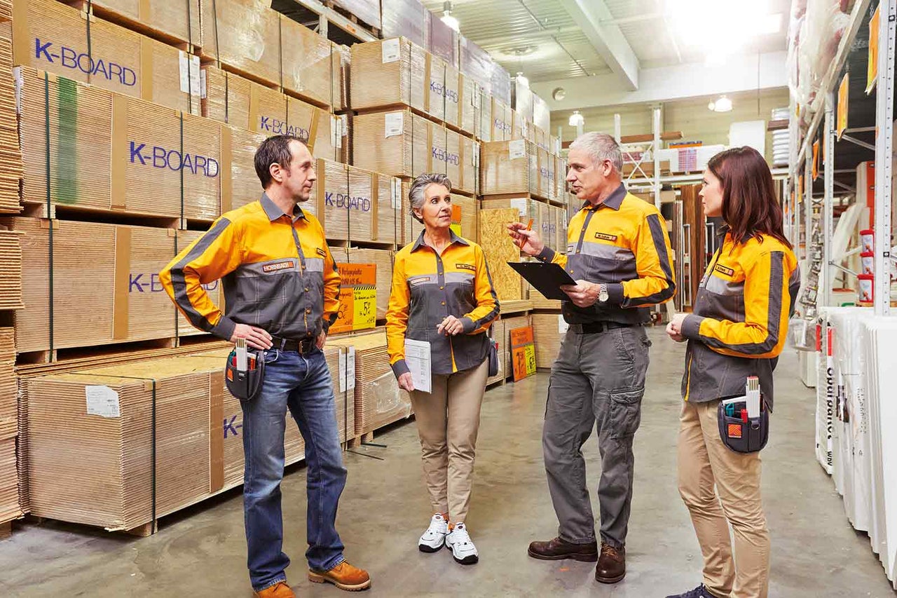 Čtyři zaměstnanci společnosti Hornbach diskutují před regálem s dřevěnými panely.