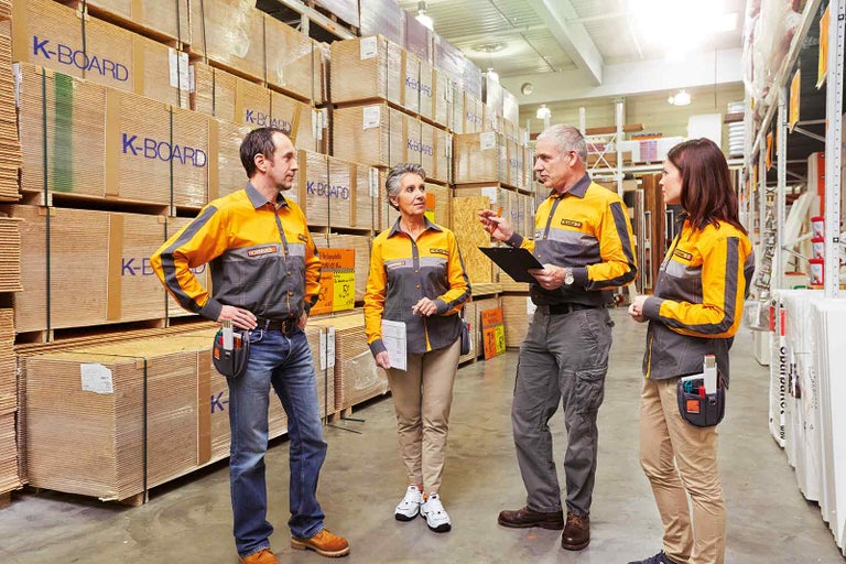 Čtyři zaměstnanci společnosti Hornbach diskutují před regálem s dřevěnými panely.