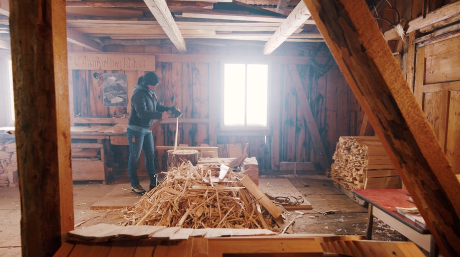Interiér dílny s dřevěnými stěnami a ženou pracující se dřevem.