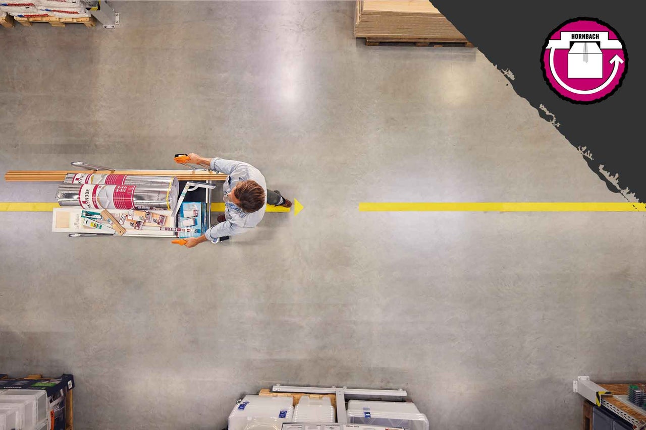 Pohled shora na muže tlačícího nákupní vozík s plechovkami barev a dřevěnými lištami po podlaze hobbymarketu Hornbach. Logo Hornbach