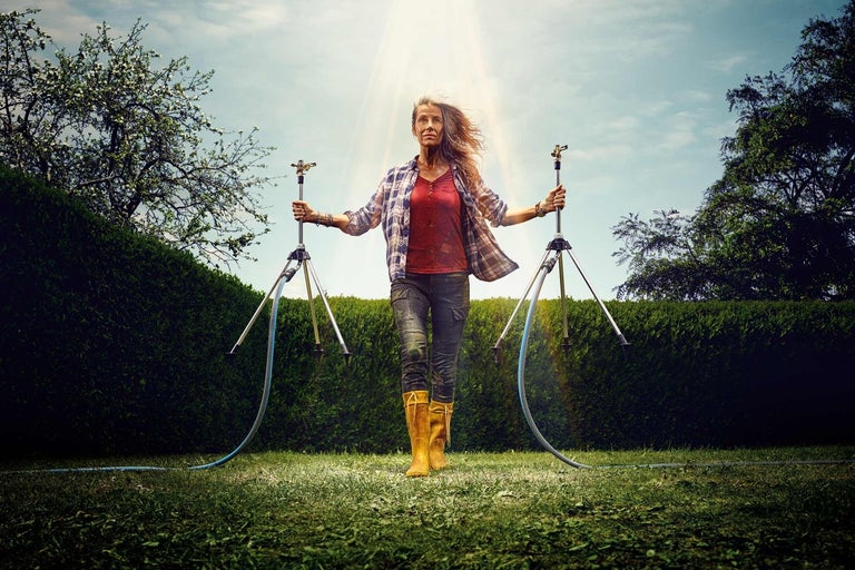 Žena se dvěma zavlažovači trávníku na stativech na zahradě