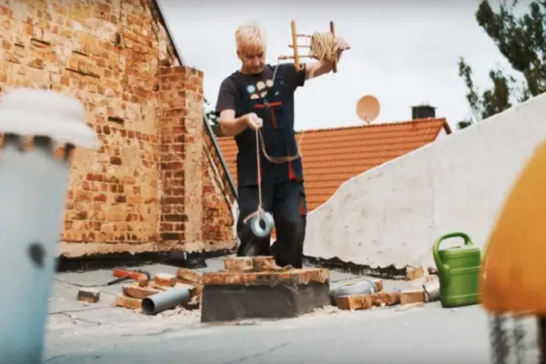 Kominík při práci na střeše s nářadím a materiálem pro opravu komína.