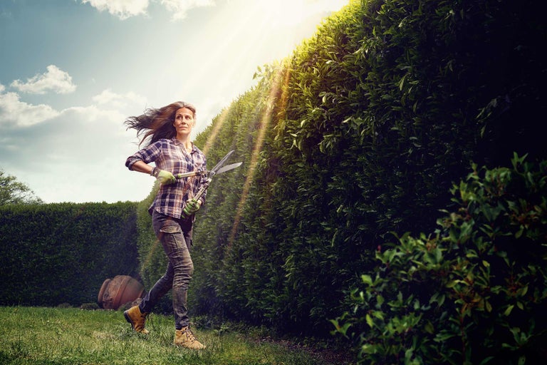 Žena běží s nůžkami na živý plot vedle živého plotu