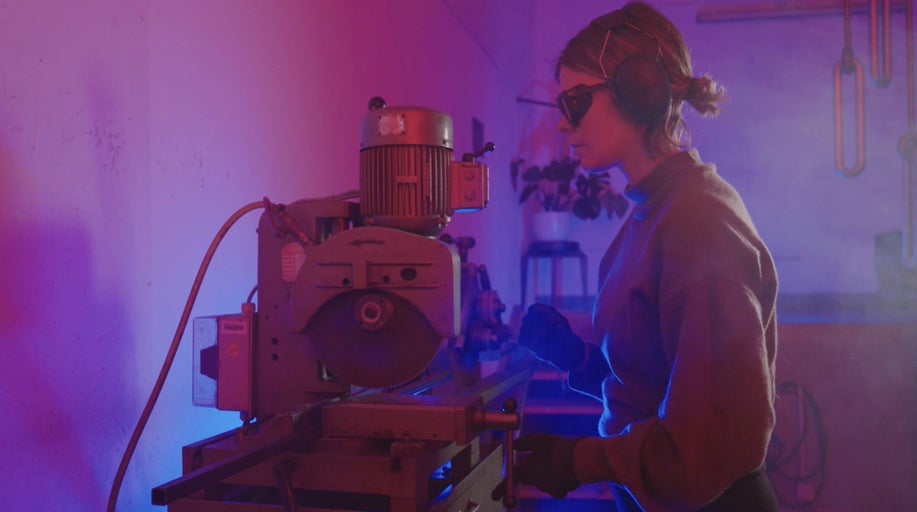 Žena obsluhuje pilu na kovy s ochrannými brýlemi a ochranou sluchu.