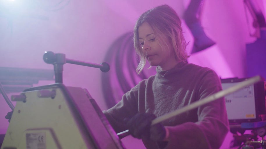 Žena obsluhuje stroj na zpracování kovů v dílně.