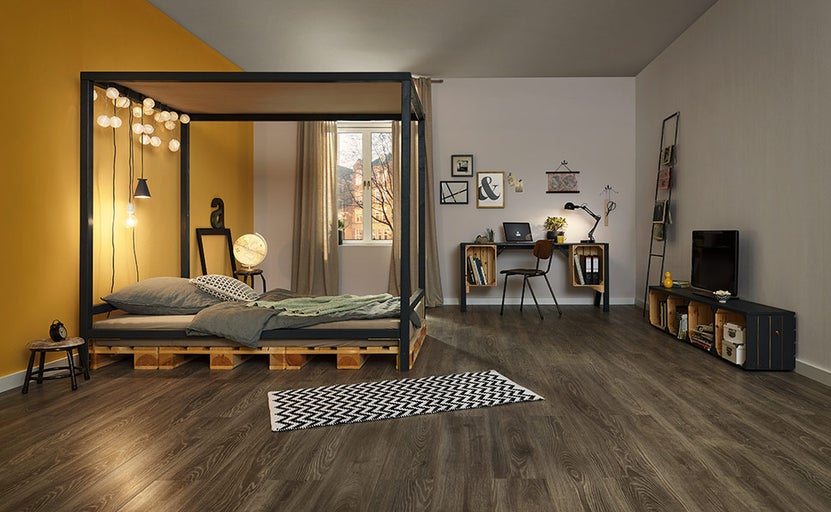 Ukázka uspořádání s postelí na paletách, psacím stolem a policemi v obývacím pokoji.