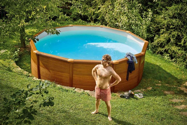 Kulatý bazén s dřevěným obkladem a stojícím mužem na zahradě