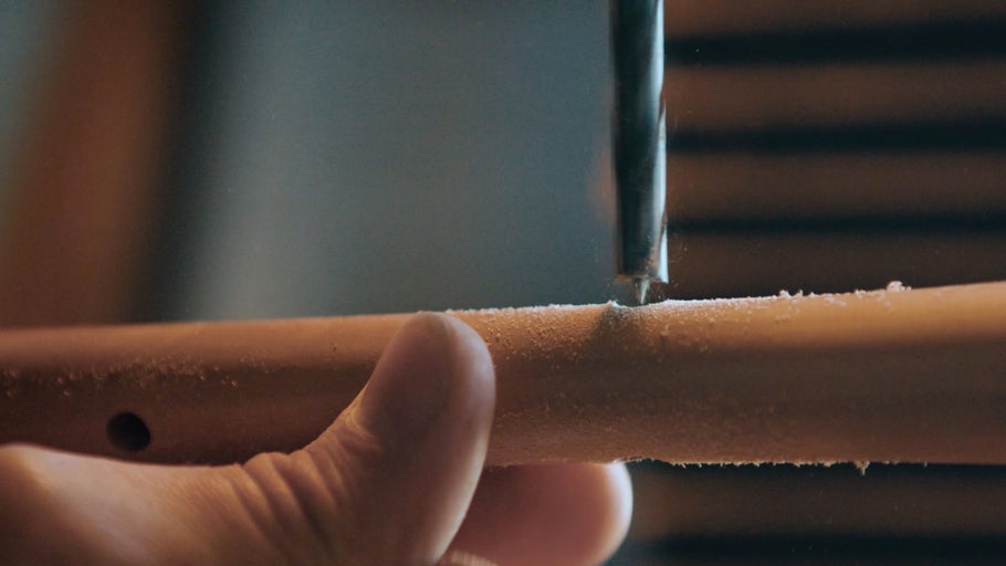 Vrták vrtá otvor do kusu dřeva, který drží ruka.