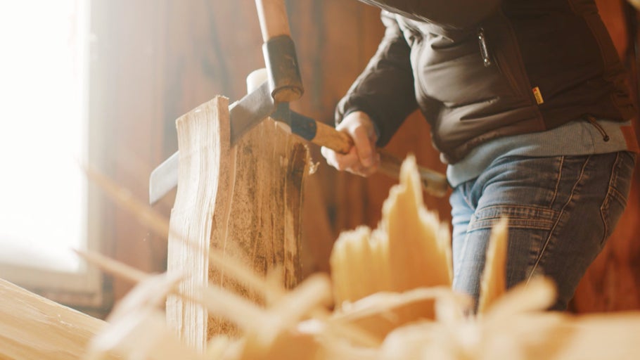 Osoba štípe dřevo pomocí klínu a kladiva