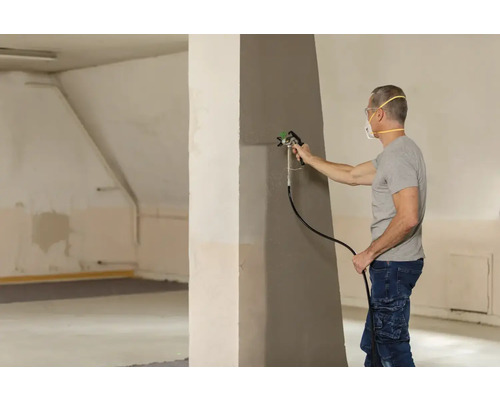 Muž maluje stěnu pomocí stříkací pistole