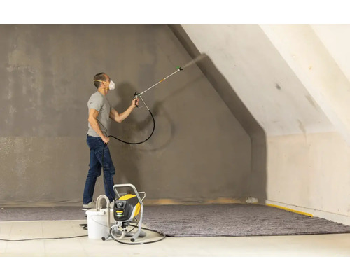 Muž stříká barvu pomocí stříkací pistole na stěnu v místnosti.