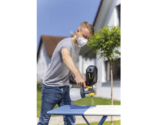 Muž používá stříkací pistoli k natírání stolu venku.