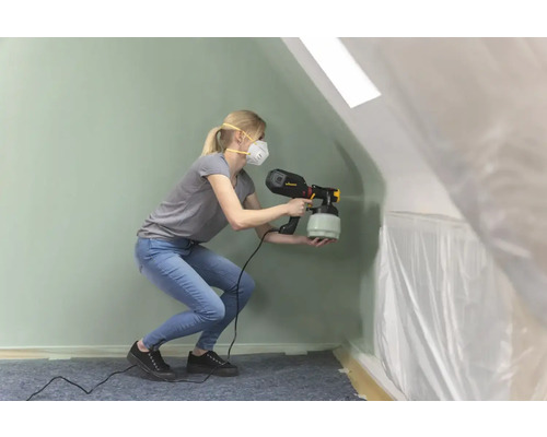 Žena používá stříkací pistoli v místnosti zakryté fólií.